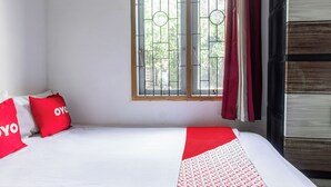 A bed with a white and red patterned bedspread, two red pillows with 'YOYO' text, a window with metal bars, and a wooden wardrobe. - Hotel O Lestari Homestay (Kotaraja)