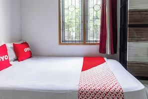 A bed with a white and red patterned bedspread, two red pillows with 'YOYO' text, a window with metal bars, and a wooden wardrobe.