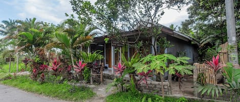 Una casa con porche, rodeada de exuberante vegetación y plantas tropicales.