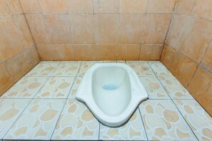 A small, square-shaped toilet with a white seat and a blue drain hole, surrounded by patterned tiles. - Hotel O Lestari Homestay (Kotaraja)