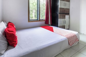 A single bed with white bedding and red accents, a window with metal bars, and a radiator on the wall.