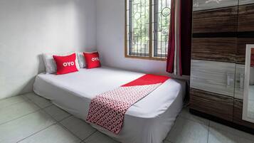 A single bed with a white mattress and red accents, a window with metal bars, and a wooden wardrobe.