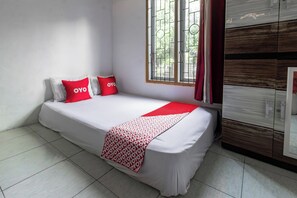 A single bed with a white mattress and red accents, a window with metal bars, and a wooden wardrobe.