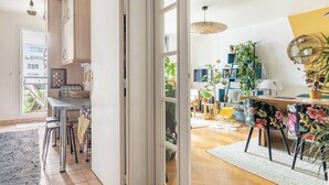 A modern kitchen with a large window, a dining area with a floral tablecloth, and a view of a cityscape. - Large Two-bedroom Flat to Rent in Paris,100m From Beautiful Buttes Chaumont Parc (Paris)