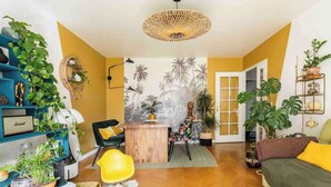 A cozy living room with a wooden coffee table, a black sofa, and a yellow chair. There are plants on shelves and a large plant next to the sofa. - Large Two-bedroom Flat to Rent in Paris,100m From Beautiful Buttes Chaumont Parc (Paris)