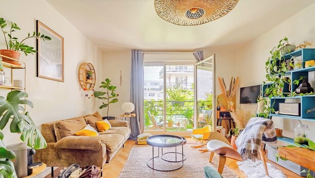 A cozy living room with a sofa, a coffee table, and a TV. There are plants and a window with a view of the outside. - Large Two-bedroom Flat to Rent in Paris,100m From Beautiful Buttes Chaumont Parc (Paris)