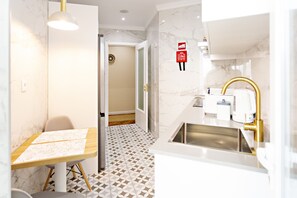 A modern bathroom with a sink, toilet, and shower area. There is a table with papers on it and a chair. The floor has a geometric tile pattern.