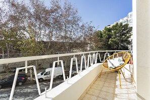 A balcony with a wicker chair and a view of parked cars and trees.