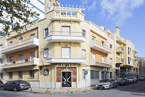 A multi-story residential building with balconies, a central entrance with a distinctive door, and parked cars along the street. - Ideal for 6px, modern and cosy (Faro)
