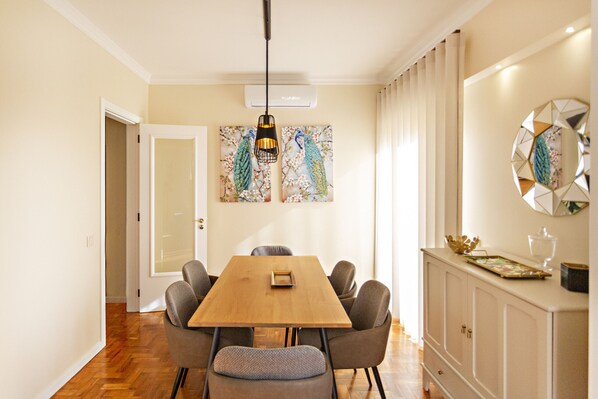 A dining area with a wooden table, six chairs, a pendant light, a wall-mounted mirror, and a decorative piece above the mirror.