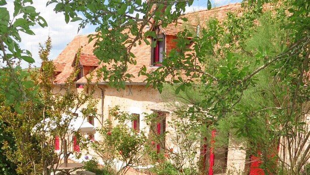 A garden with wooden lounge chairs and a table, surrounded by greenery and a building with red accents. - Gîte Écoconçu Charmant Proche zoo de la Flèche : Idéal Famille (CLERMONT CREANS)