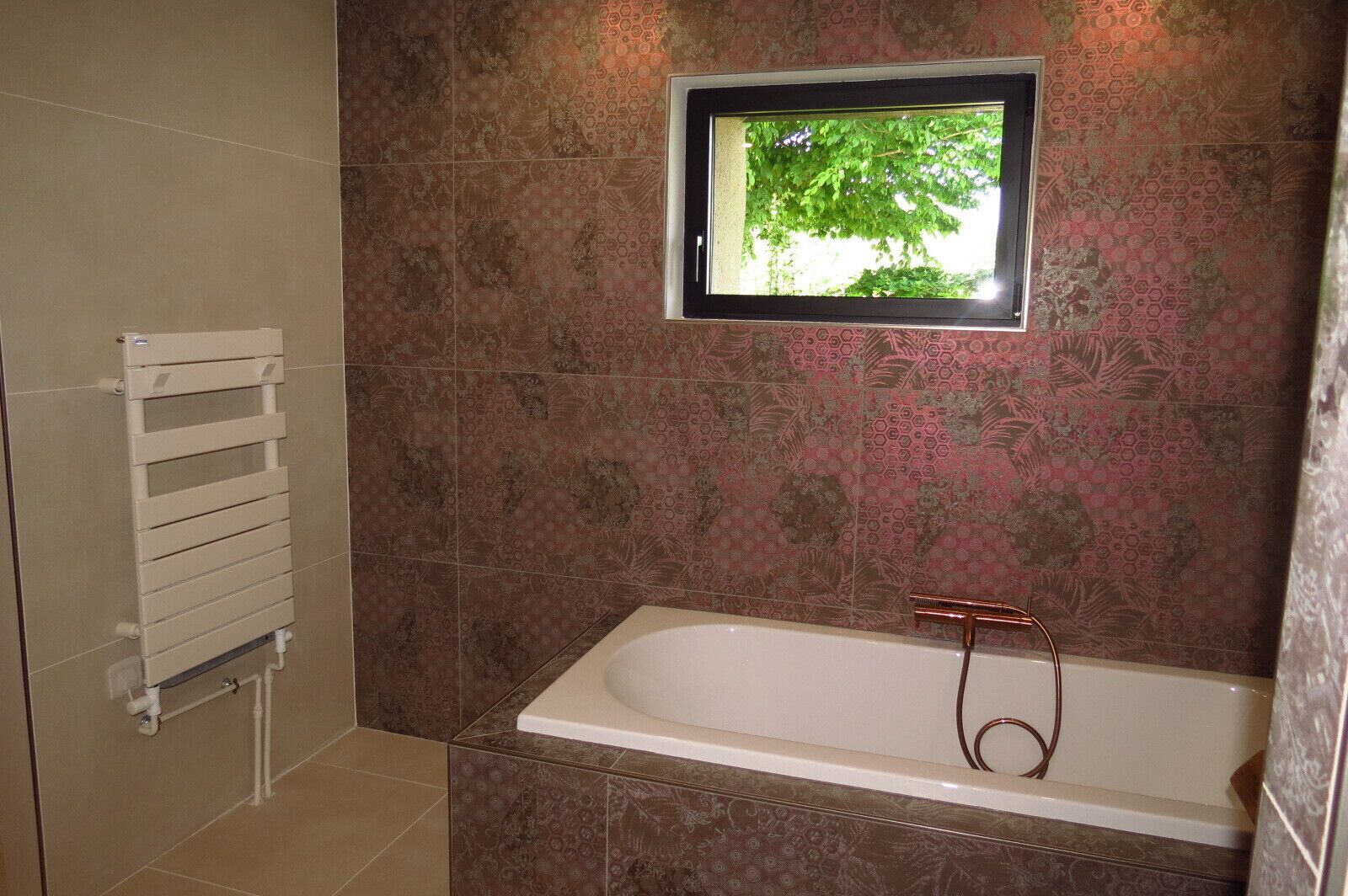 Une salle de bain avec une baignoire, une fenêtre donnant sur un espace verdoyant et un porte-serviettes.