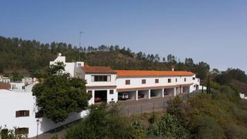 Un edificio blanco con techo de tejas rojas, varios garajes y un paisaje montañoso de fondo.