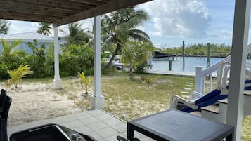 Un espace extérieur abrité, doté d’une table et de chaises, offrant une vue sur un plan d’eau et bordé de palmiers.