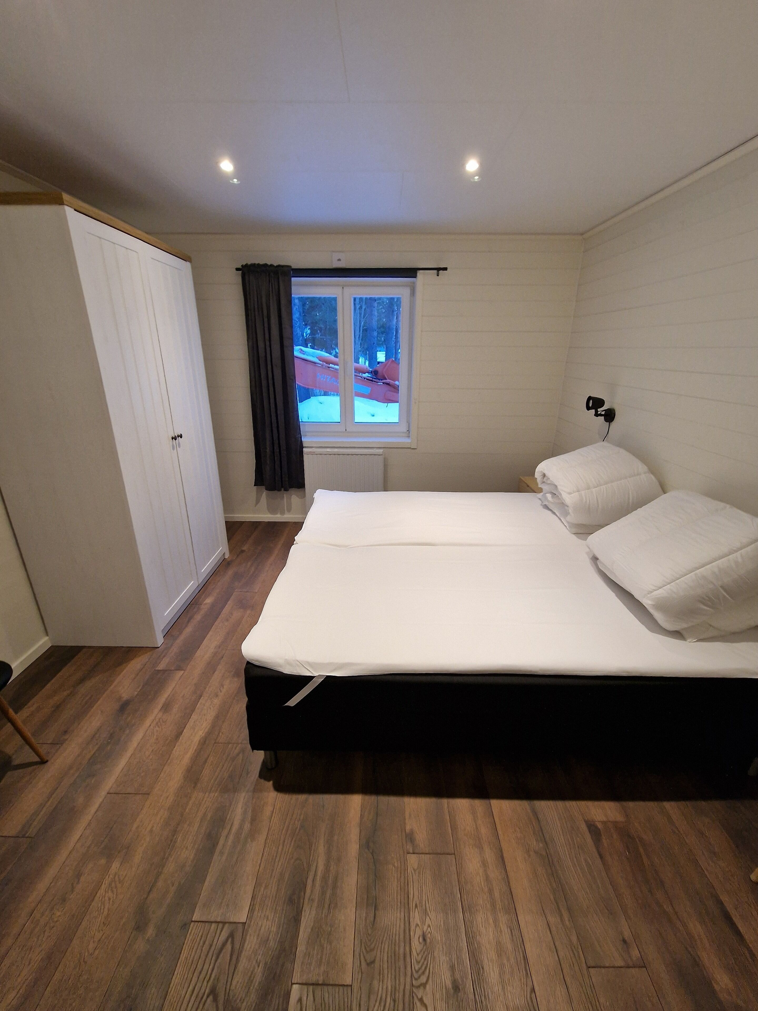 Un dormitorio con una cama grande, un armario, una ventana con cortinas y un radiador.