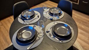 A modern kitchen with dark cabinetry, a dining table set for four, and a window with a view of the outside. - Bryggerihusen (Kåbdalis)