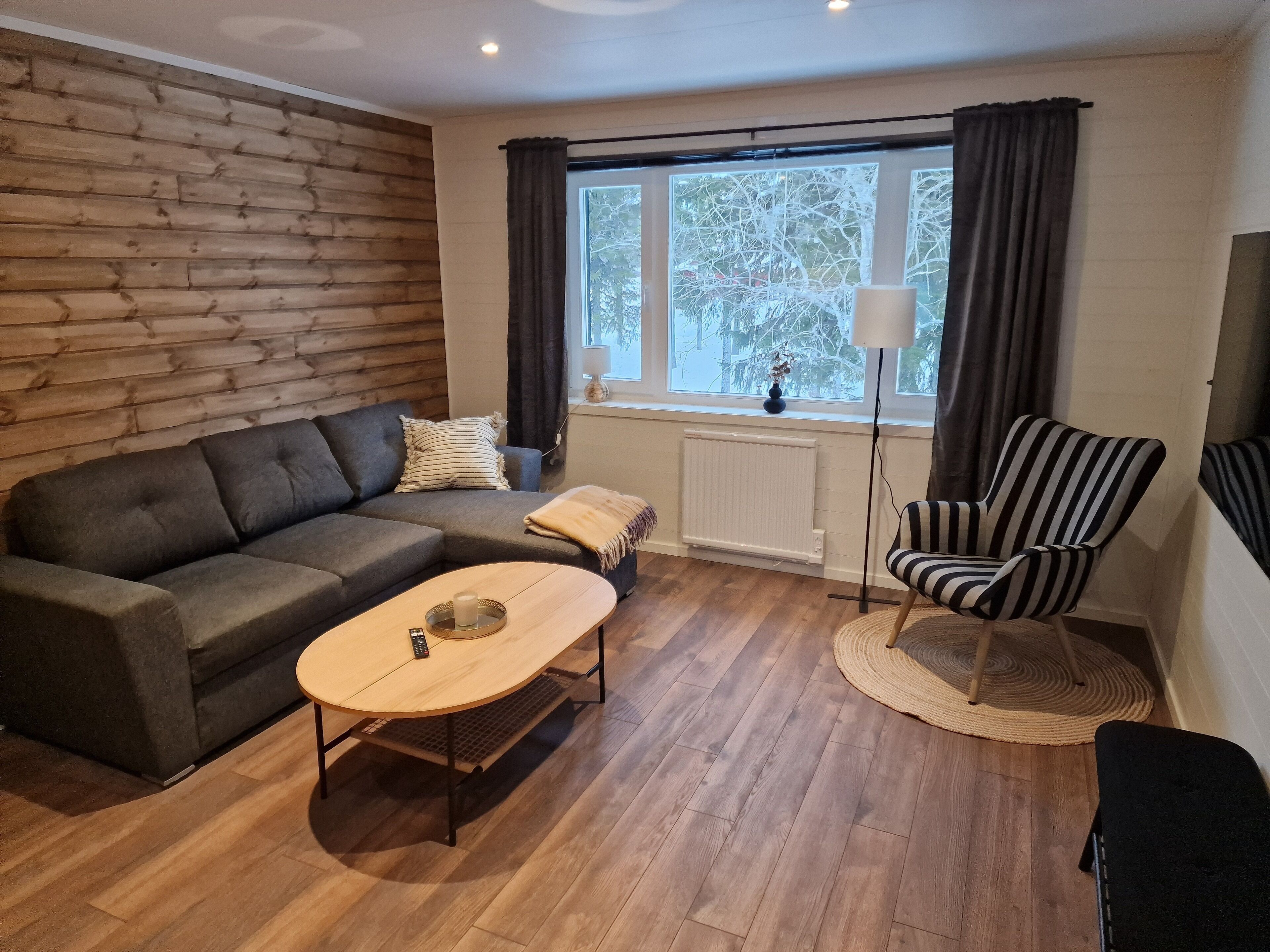 Una sala de estar acogedora con un sofá modular, una mesa redonda de centro, un sillón a rayas y un ventanal con cortinas.