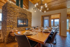 A dining area with a stone wall, a fireplace, and a long wooden table set for dining.