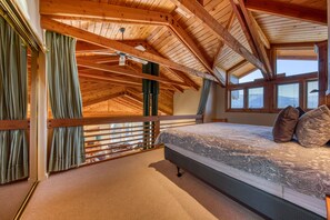 A bedroom with a sloped ceiling, a large bed with patterned bedding, and a view of the outdoors through windows.