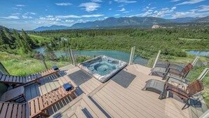 A deck with a hot tub, lounge chairs, and a view of a lake and mountains. - Cliff Cabin | Hot Tub | Spectacular Views (Fairmont Hot Springs)