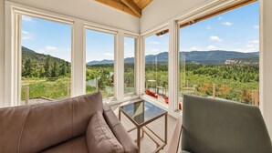 A room with a large window, a glass table, and a sofa. - Cliff Cabin | Hot Tub | Spectacular Views (Fairmont Hot Springs)