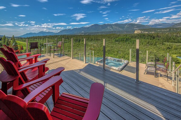 A deck with red Adirondack chairs, a hot tub, and a scenic mountain view.
