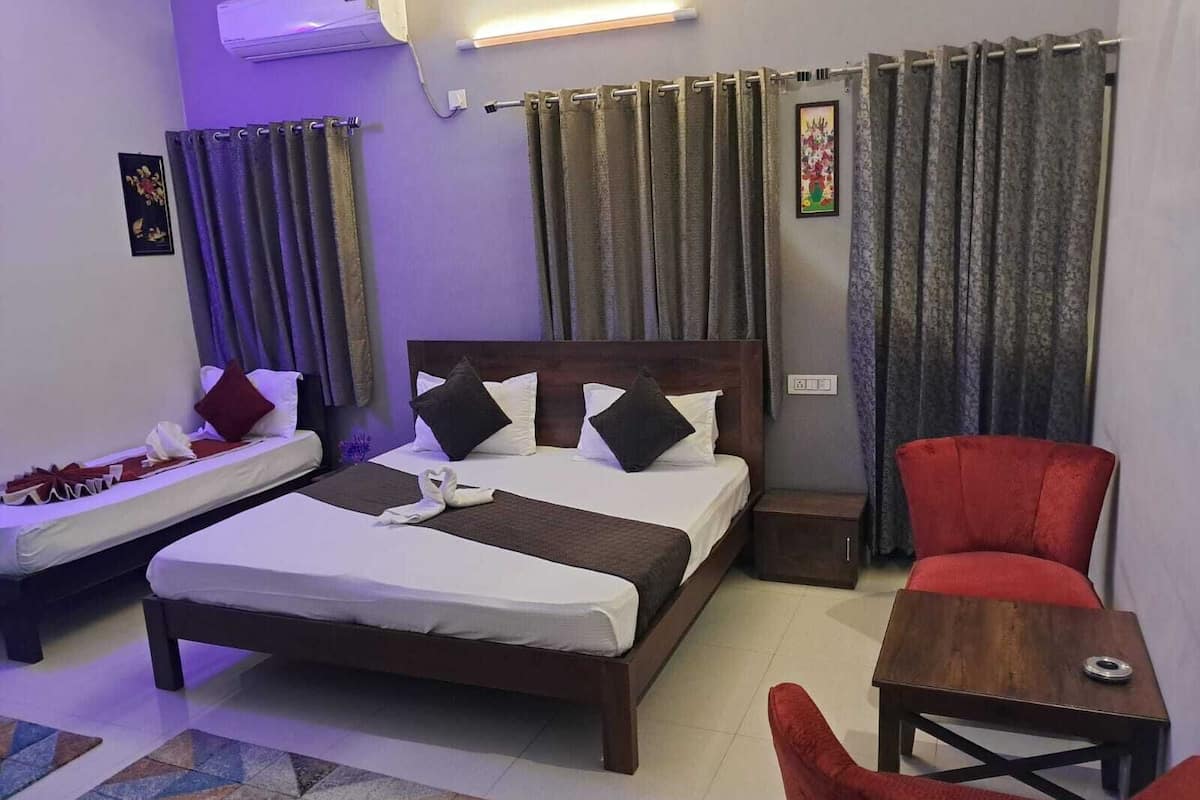 A hotel room with a bed, a small table, a red chair, and a patterned rug.