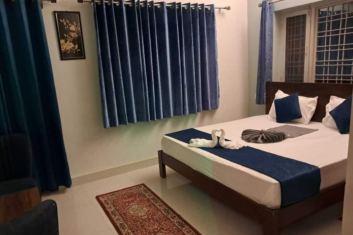 A neatly made bed with blue bedding and pillows, a patterned rug, and a framed picture on the wall.