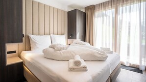 A modern hotel room with a large bed, a bedside table, and a view of the outdoors through sheer curtains. - TOP 5 - Luxuriöses Apartment in der Tiroler Zugspitzarena (Berwang)