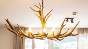 A dining area with a chandelier made of antlers, a glass bowl on a wooden coaster, and a view of the outdoors through large windows. - TOP 5 - Luxuriöses Apartment in der Tiroler Zugspitzarena (Berwang)