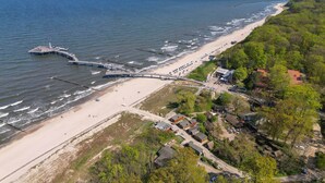An aerial view of a coastal area with a beach, a pier, and a cluster of buildings. - Cozy vacation apartment by the sea with balcony, WiFi & parking space (Koserow)