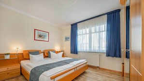 A hotel room with a wooden bed, bedside tables, a window with curtains, and artwork on the wall. - Cozy vacation apartment by the sea with balcony, WiFi & parking space (Koserow)