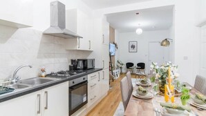 A modern kitchen with white cabinets, a stove, and a sink. There is a dining area with a wooden table set for two.