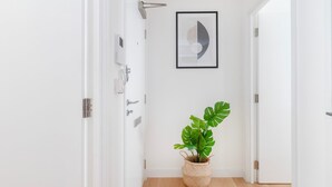 A hallway with white walls, a framed abstract artwork, and a potted monstera plant.