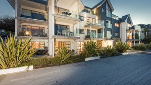 Un immeuble résidentiel moderne à plusieurs étages, doté de balcons, de grandes fenêtres et d’une allée pavée.