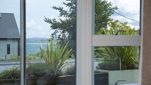 Une vue à travers une fenêtre, avec une maison, un jardin et une étendue d’eau en arrière-plan.
