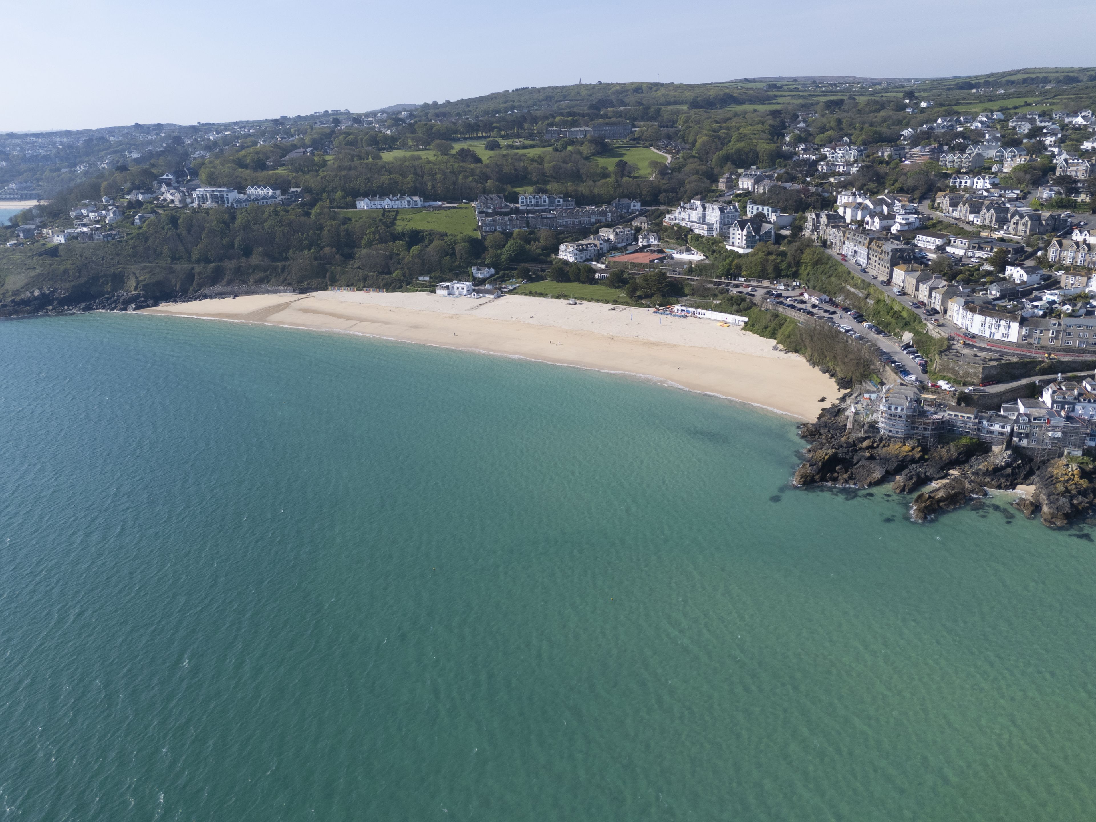 An aerial view of a coastal town with a sandy beach, residential buildings, and a rocky shoreline.