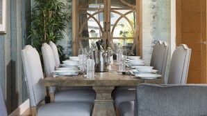 Une table à manger dressée avec des assiettes, des verres et des couverts, entourée de chaises rembourrées ornées de clous métalliques.
