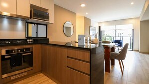 A modern kitchen with a central island, built-in oven, microwave, and a dining area with a blue chair. - w* | Homey 3BR with Balcony in Premium Miraflores (Miraflores)