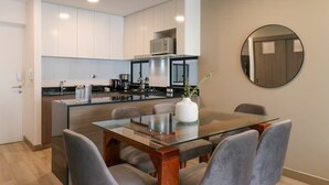 A modern kitchen with white cabinets, a stainless steel refrigerator, and a glass dining table with grey chairs. - w* | Homey 3BR with Balcony in Premium Miraflores (Miraflores)