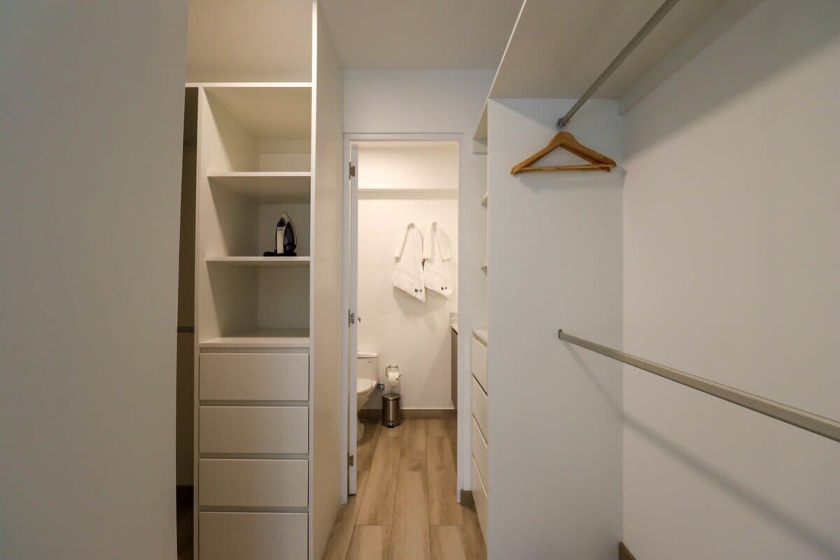 A narrow hallway with a closet on the left, a hanging rack on the right, and a door leading to a bathroom.