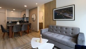 A modern living room with a grey sofa, a dining area with a table and chairs, and a kitchen in the background. - w* | Homey 3BR with Balcony in Premium Miraflores (Miraflores)