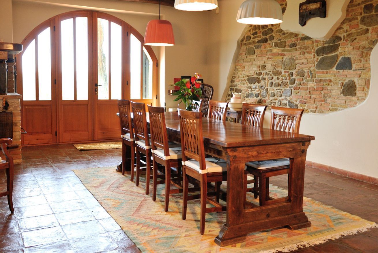 A dining area with a wooden table and chairs, a patterned rug, and a stone wall.