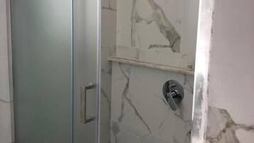 Une salle de bain avec une douche à parois de verre, des murs en marbre et un sol carrelé.