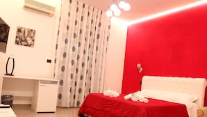 A hotel room with a red accent wall, a bed with white bedding, a desk with a computer, and a patterned curtain. - BEAUTY HOUSE (Reggio Calabria)