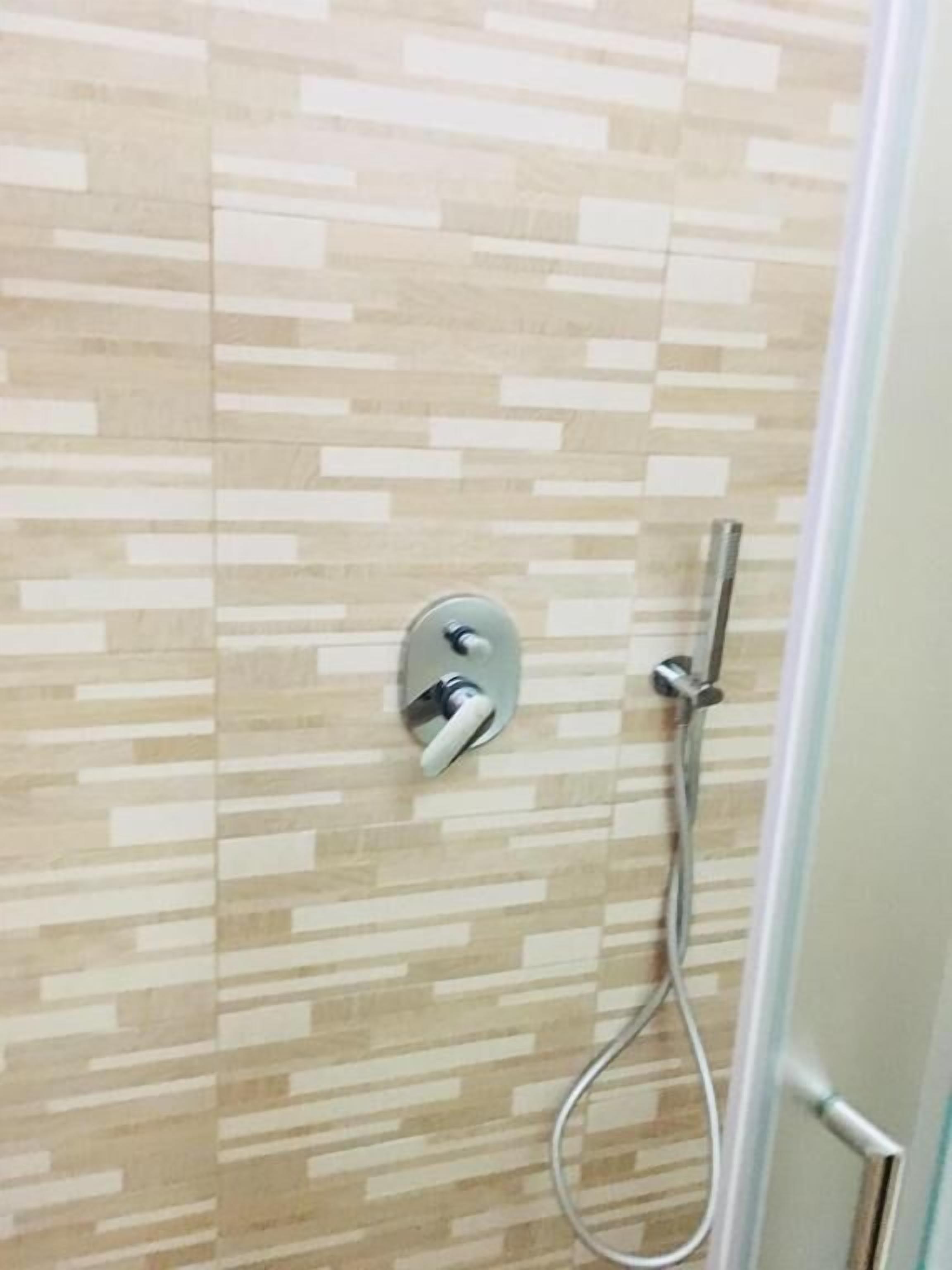 A shower with a modern design, featuring a tiled wall and a handheld showerhead.