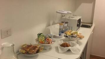 A kitchenette with a microwave, coffee maker, and various food items on the counter.