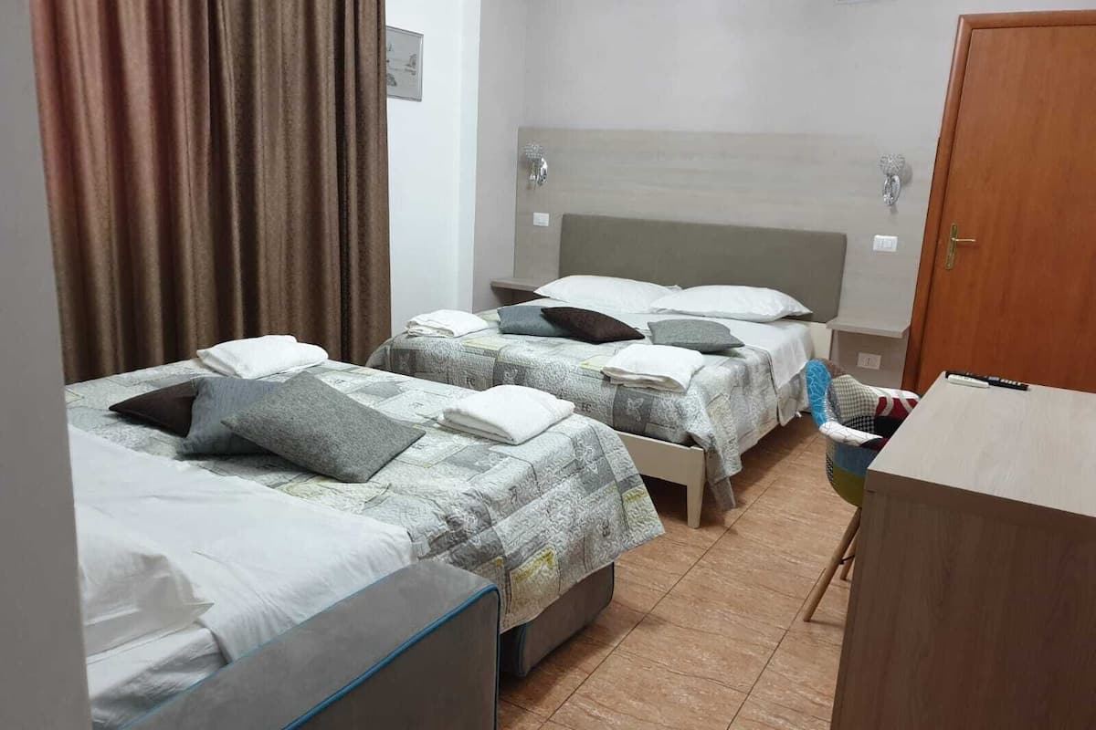 A hotel room with two single beds, a wooden wardrobe, a small table, and a curtain.