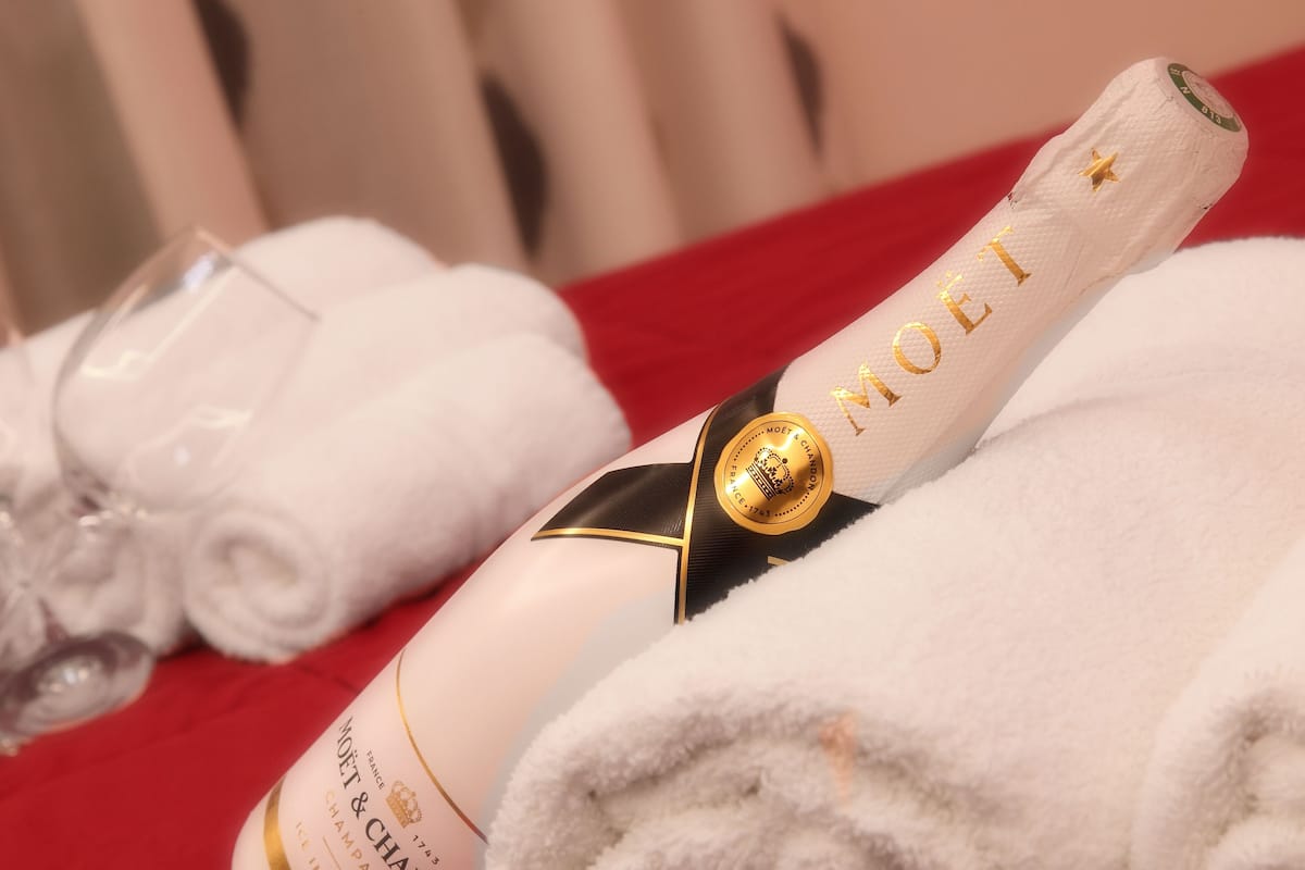 A bottle of Moët & Chandon champagne, a glass, and rolled towels on a red surface.