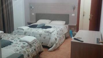 Una camera d'albergo con due letti, una scrivania in legno e l'ingresso del bagno.